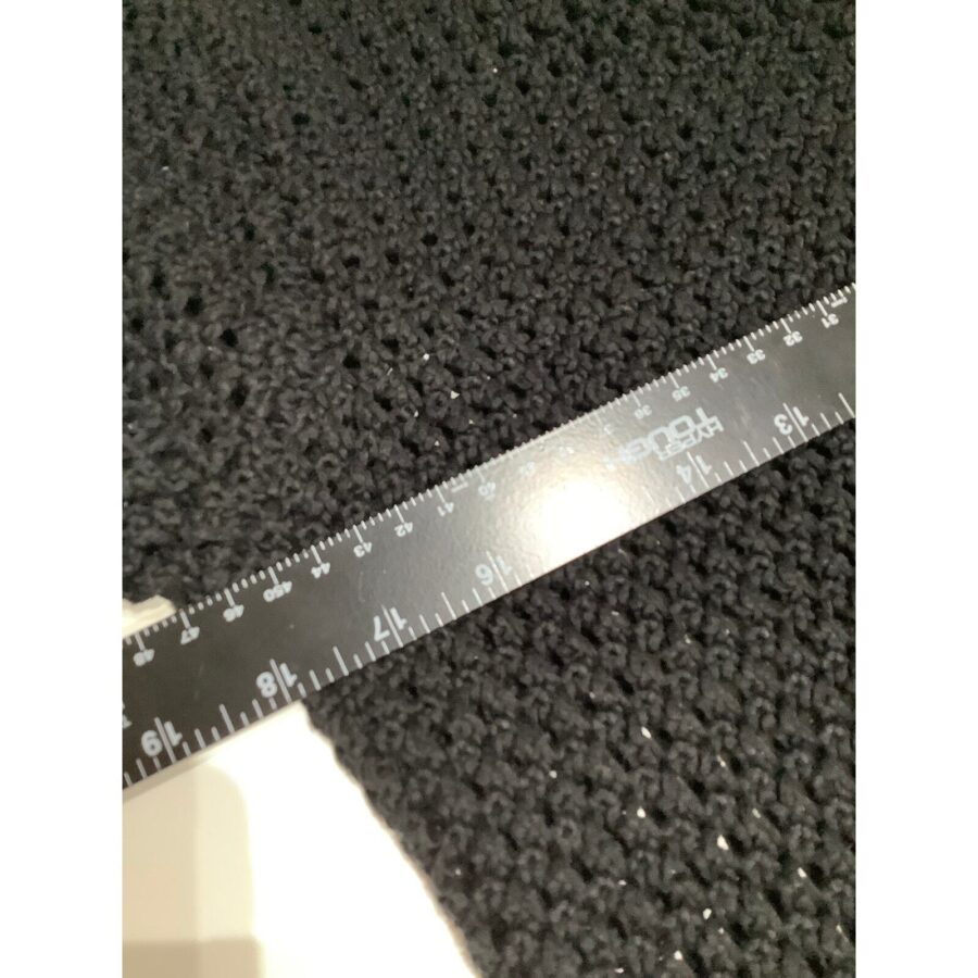 A black crocheted fabric is being measured with a ruler displaying both centimeter and inch units on a white surface.