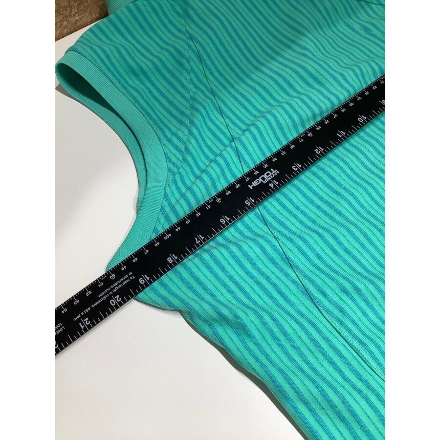 A ruler is laid across a sleeveless turquoise garment with a wavy pattern, showing measurement in inches and centimeters on a white surface.