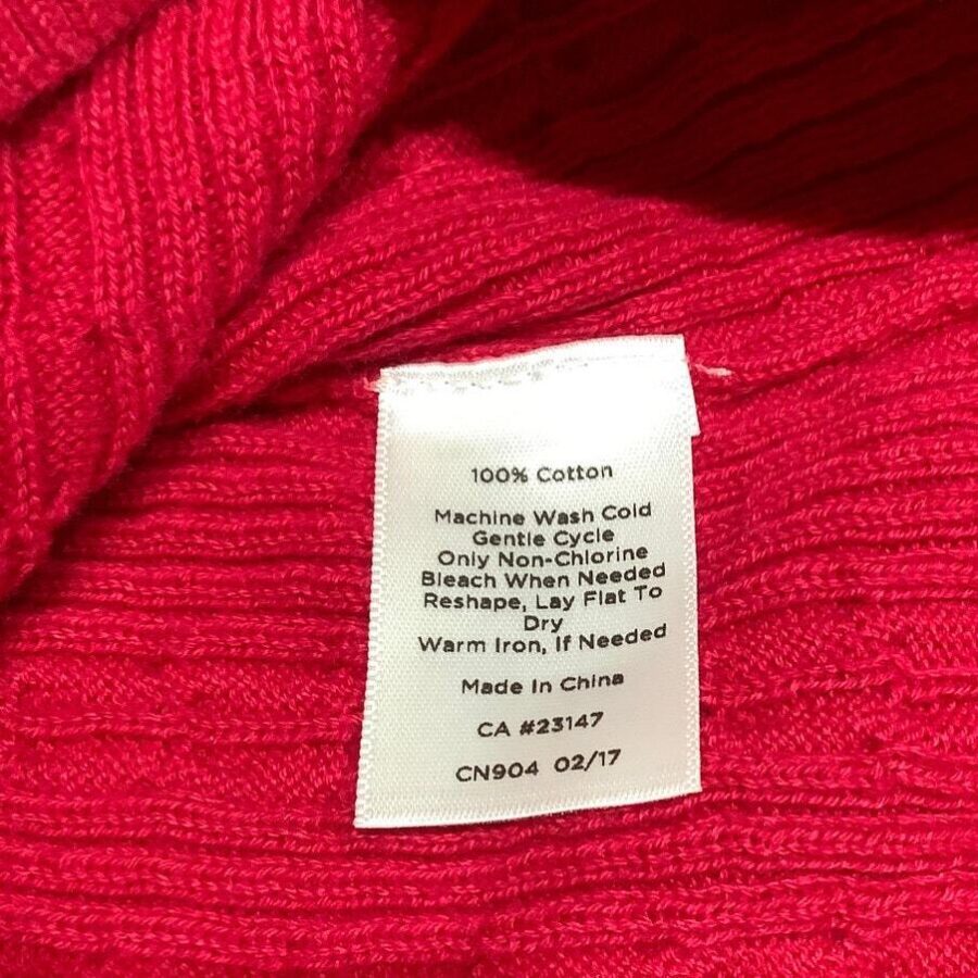 A care label for a 100% cotton garment, detailing washing instructions, is attached to a red fabric background. The item is made in China.