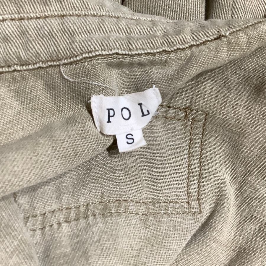 A close-up image of a beige piece of clothing with a small white label that reads "POLS" and the size "S."