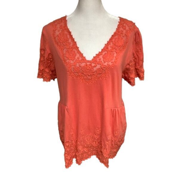 A coral-colored, lacy women's blouse on a mannequin. The blouse features intricate lace details on the sleeves, neckline, and hem.