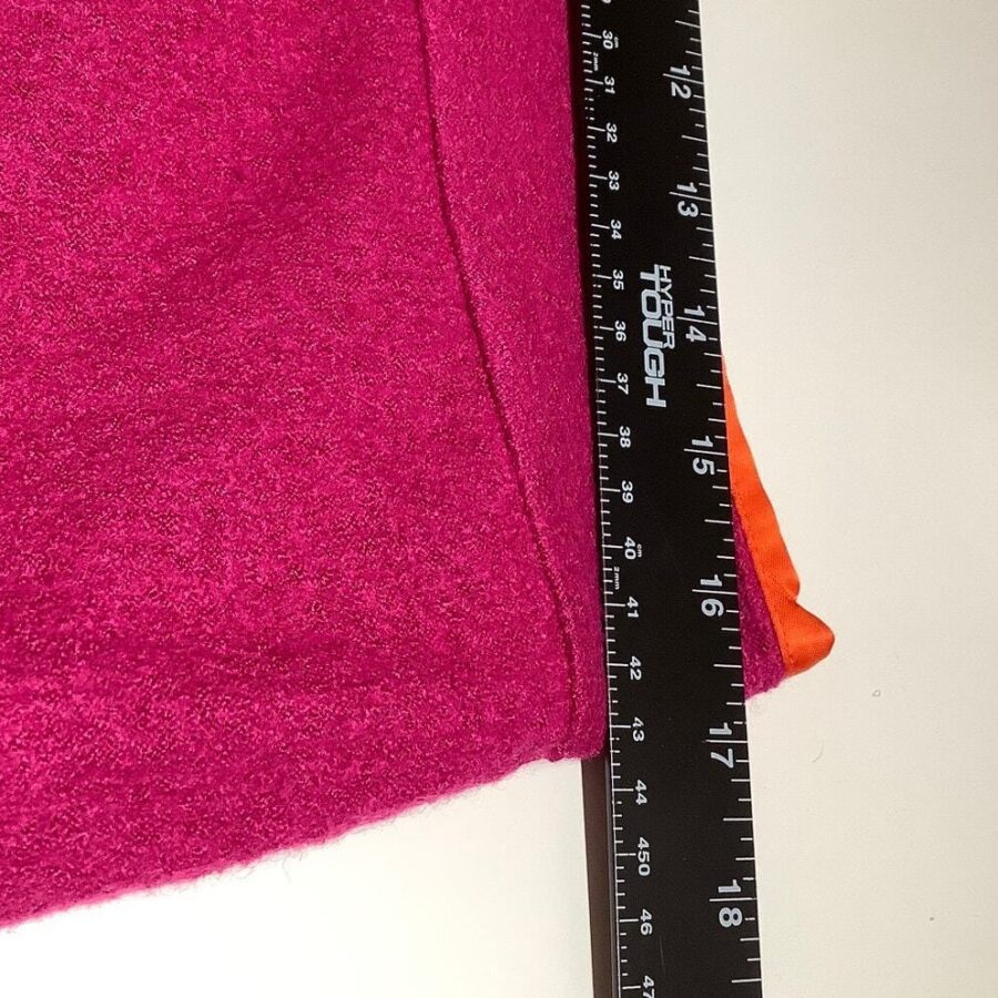 A black ruler measuring a pink textured fabric with an orange edge, placed on a white surface. The ruler reads up to 18 inches.