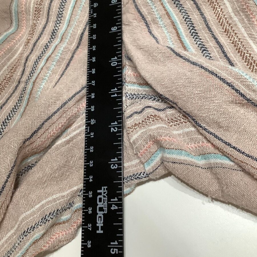 A ruler measuring a piece of beige fabric with multicolored stripes. The ruler's length is marked in both inches and centimeters, showcasing precise measurements.