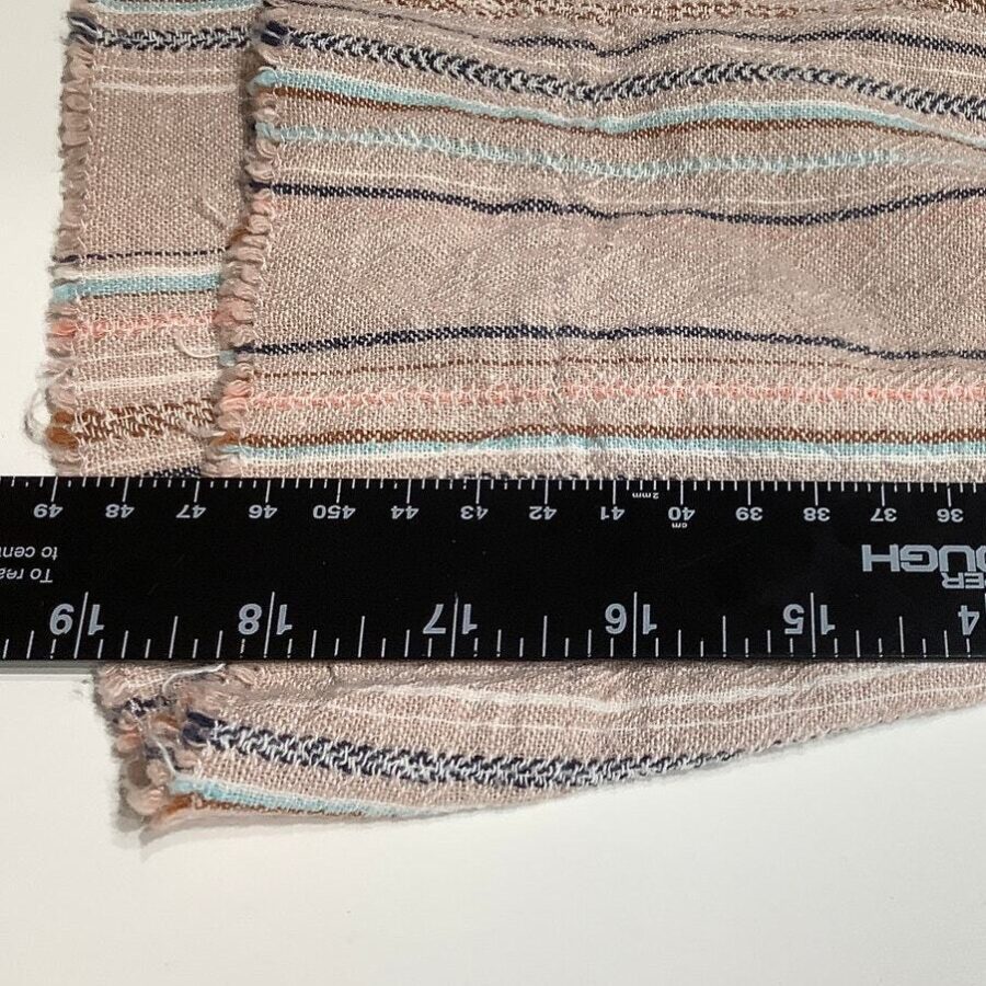 A fabric with striped patterns, featuring pastel colors, adjacent to a black ruler with inch and centimeter measurements prominently displayed.