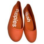 Pair of orange flat shoes with "Hush Puppies" written on the insoles, viewed from above.