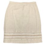 A beige skirt with intricate, symmetrical embroidery near the hem, featuring a simple yet elegant design, laid flat against a white background.