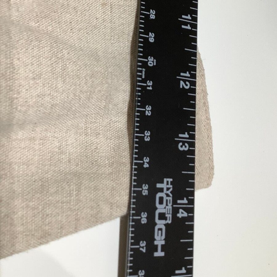 A black ruler labeled "Hyper Tough" measuring a beige fabric is placed on a white surface. The ruler's measurements are visible in inches.