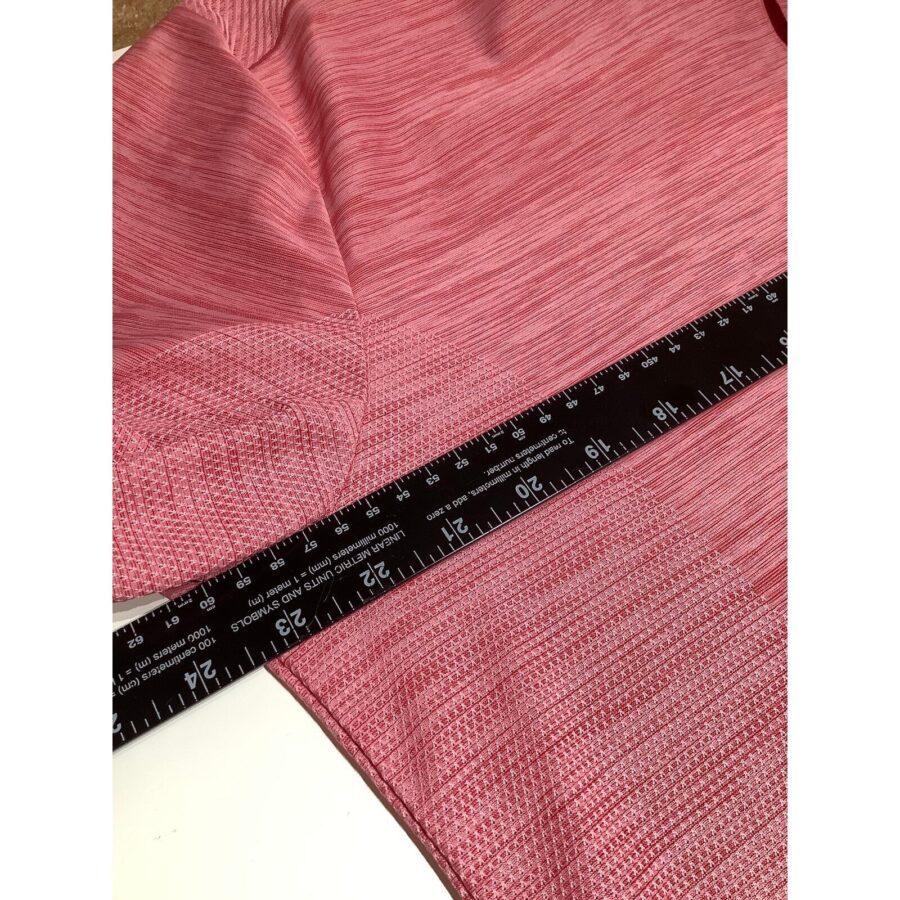 A close-up of pink fabric with a black ruler measuring it. The fabric appears textured, and the ruler shows measurements in inches and centimeters.