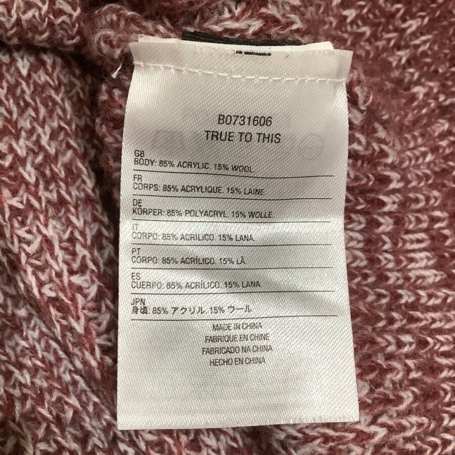 A multi-language clothing label indicates the garment composition (85% acrylic, 15% wool) with "Made in China" in several languages, attached to a maroon knit fabric.