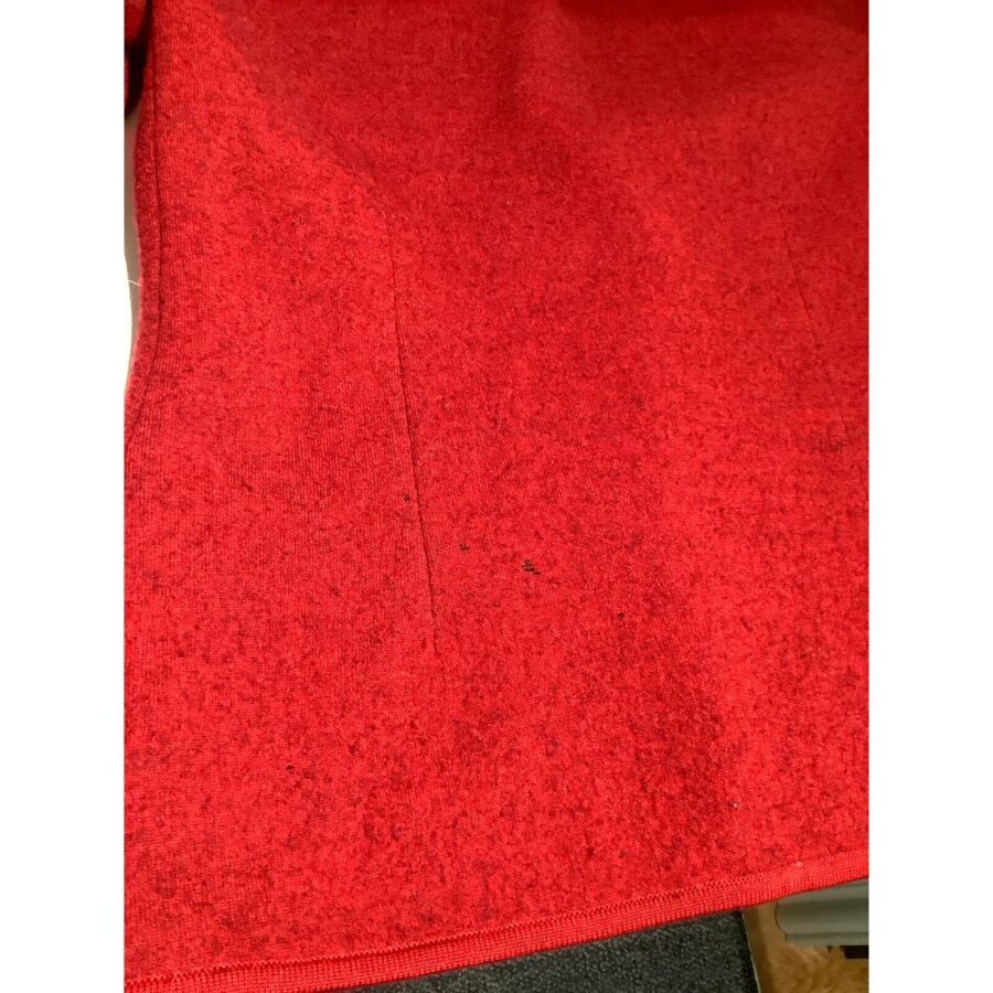 Close-up of a red textured fabric with some visible small black specks. The fabric appears to be flat and evenly colored.