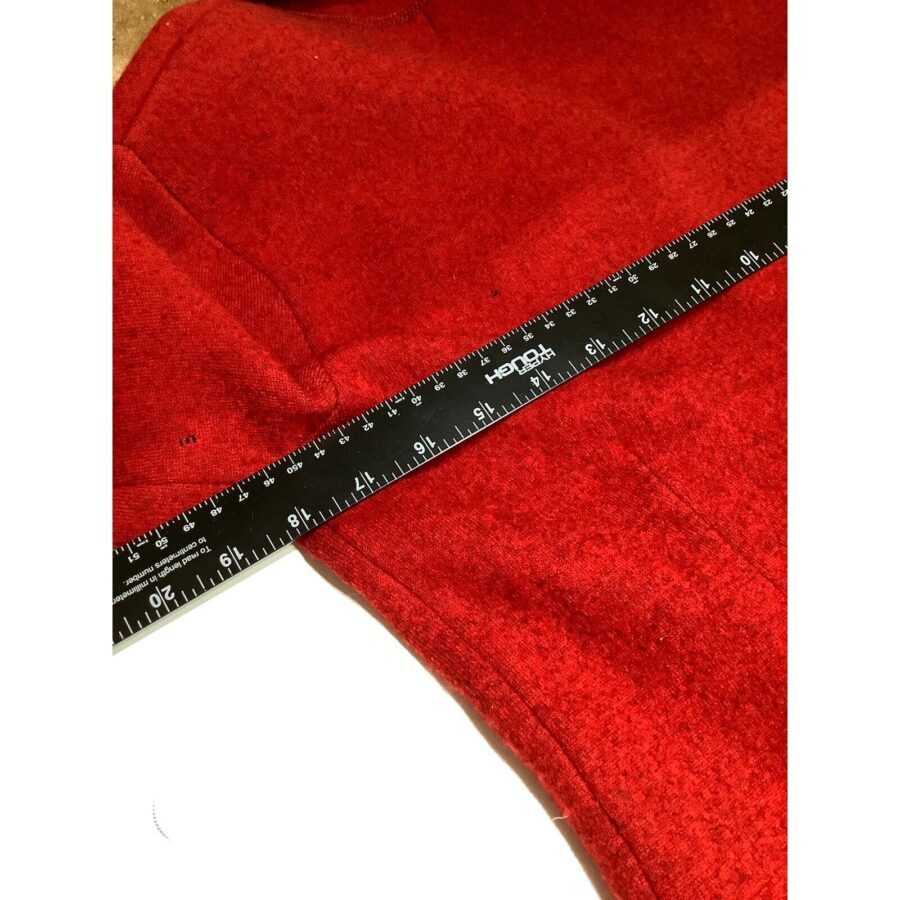 A black ruler is placed on a red fabric. The ruler shows measurements in inches and centimeters, with small marks indicating precise measurements.