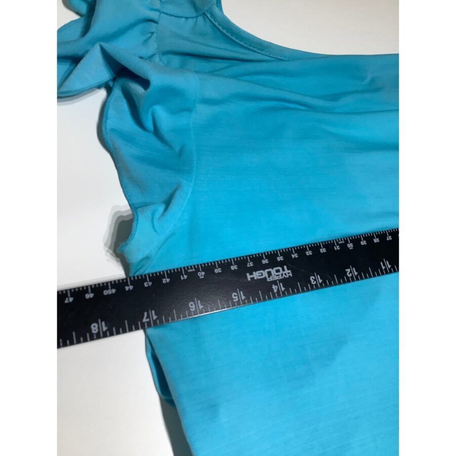 A close-up image of a blue garment being measured with a black ruler on a white surface. The focus is on the fabric detail.