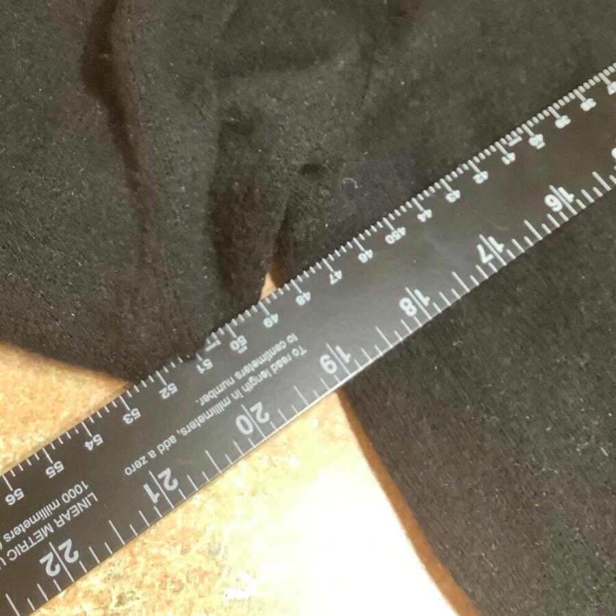 A black fabric alongside a black ruler on a tan surface. The ruler displays centimeters and inches with visible measurement markings.