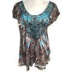 A vibrant, paisley-patterned blouse with blue accents on a mannequin, featuring decorative embroidery and a slightly asymmetrical hemline.