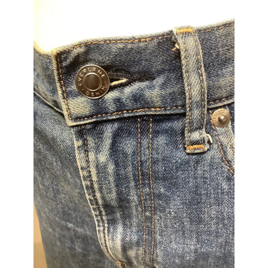 Close-up of a pair of blue jeans focused on the waistband and button, showcasing detailed stitching and denim texture.