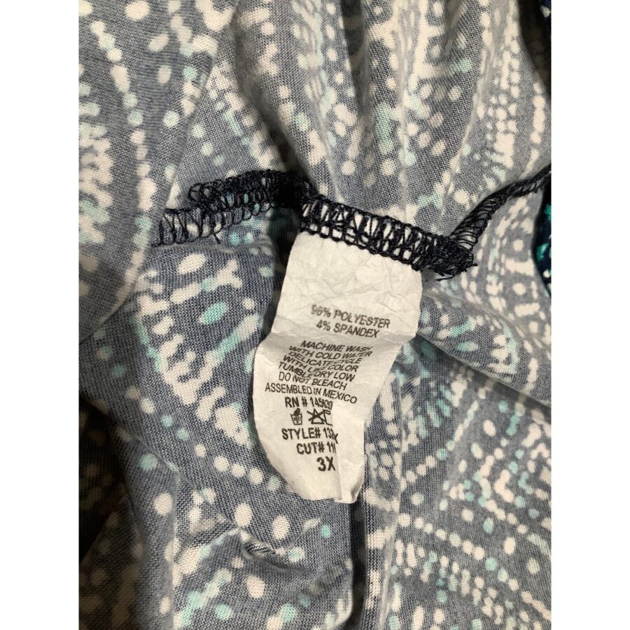 A fabric label with washing instructions and material composition, attached to a patterned piece of clothing. The label indicates a size of 3X and fabric type.