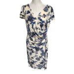 A white floral dress with blue patterns displayed on a mannequin, featuring short sleeves and a V-neckline with a ruched waist design.