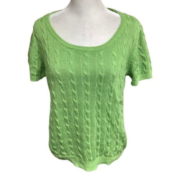 A green, short-sleeved, cable-knit sweater on a dress form. The sweater has a scoop neckline and a textured pattern throughout the fabric.