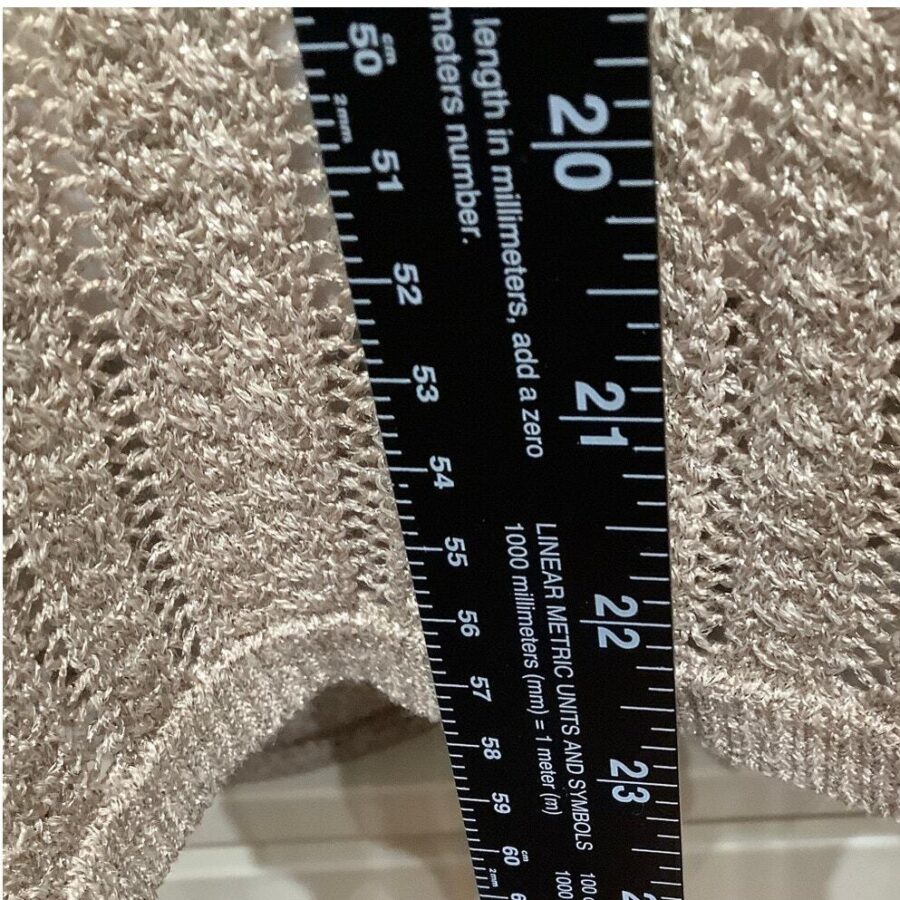 A close-up of a black ruler against a textured beige fabric, measuring approximately 21-23 centimeters on the ruler’s scale.