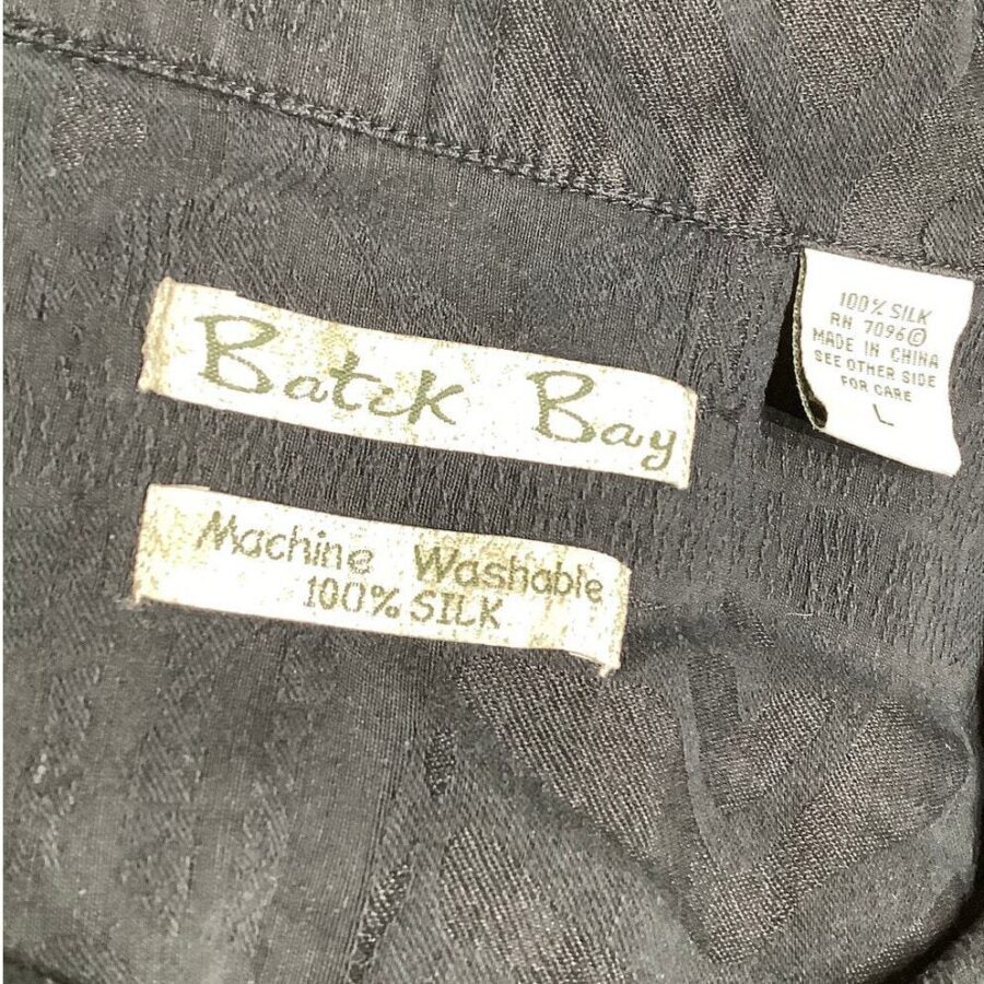 Close-up image of clothing labels on a black fabric item, indicating "Batch Bay," "Machine Washable," and "100% Silk," with instructions made in China.