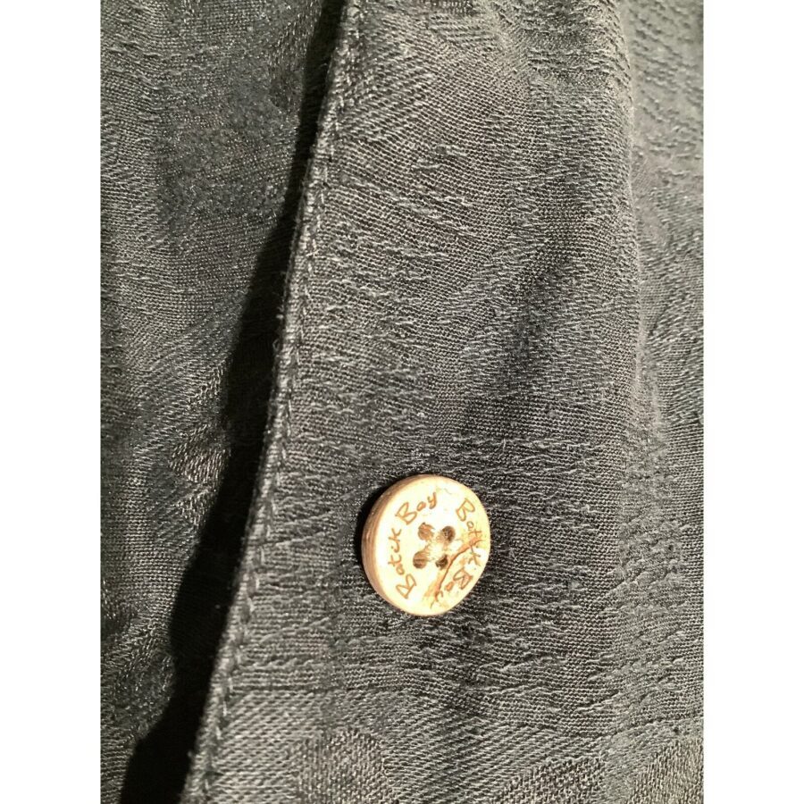 Close-up of a dark fabric featuring a white button with engraved text, "Butch Boy." The texture of the fabric is visibly detailed.