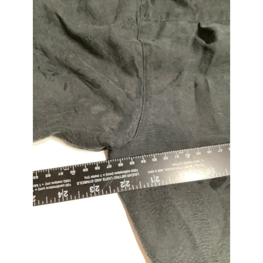 A black fabric with visible stitching is measured using a black and white ruler positioned horizontally, capturing measurements in centimeters and inches.