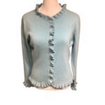 A light blue ruffled cardigan with buttons is displayed on a mannequin, showcasing its delicate design and detailing.