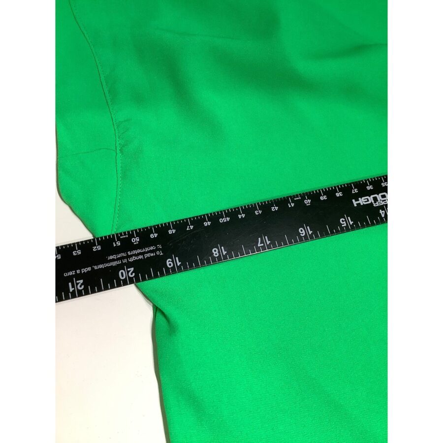 A black ruler measuring a vibrant green fabric on a white surface, showing precise measurements in inches and centimeters.