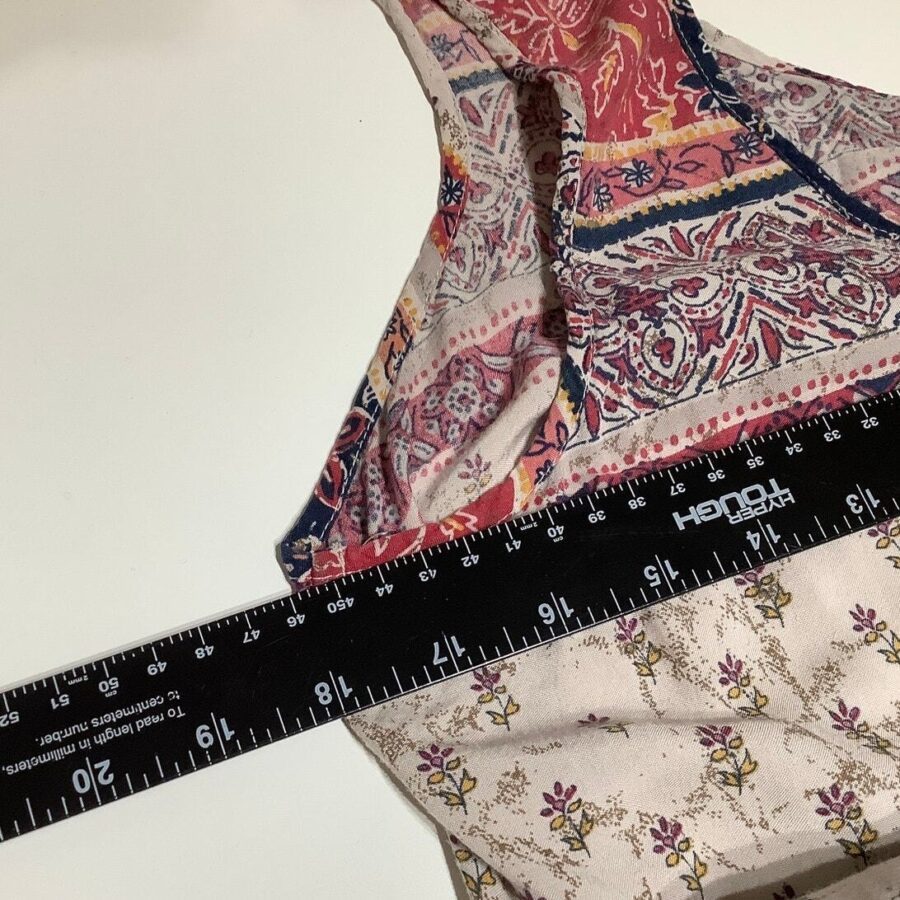 A black ruler lies on a table next to intricately patterned textile items with floral and abstract designs in shades of pink and beige.