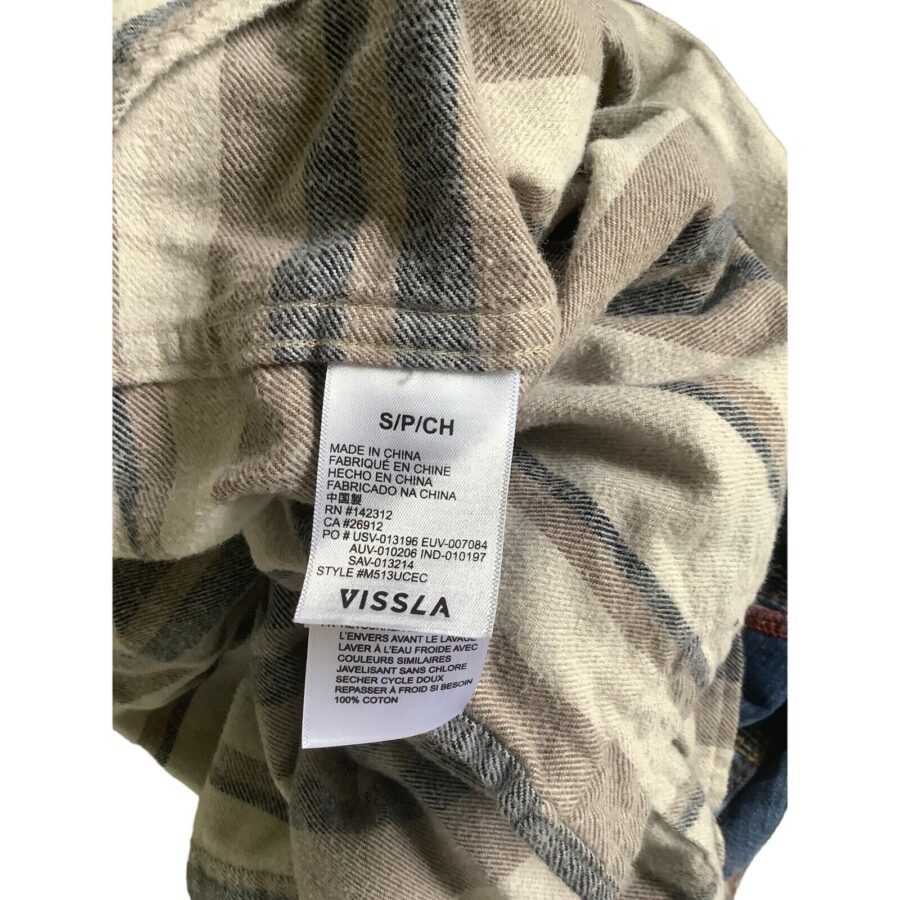 Close-up of a clothing label on a plaid fabric garment. The label shows size, material information, and the brand "VISSLA."