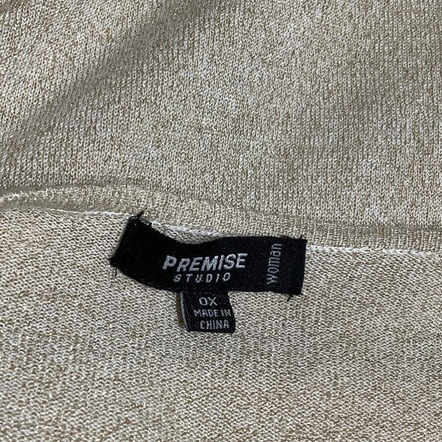 A beige fabric with a clothing label that reads "PREMISE STUDIO," "woman," "OX," and "Made in China." The fabric has visible stitching.