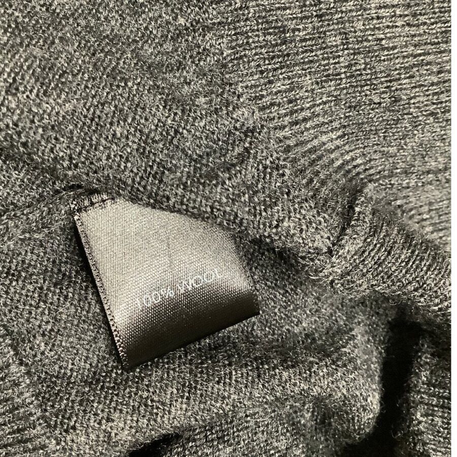 A close-up image of a gray knitted fabric with a label displaying "100% WOOL" on a black tag. The texture is clearly visible.