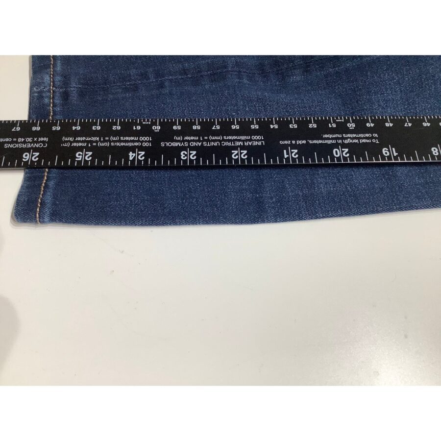 A close-up view of a blue denim pant leg being measured with a black ruler placed horizontally across the fabric.