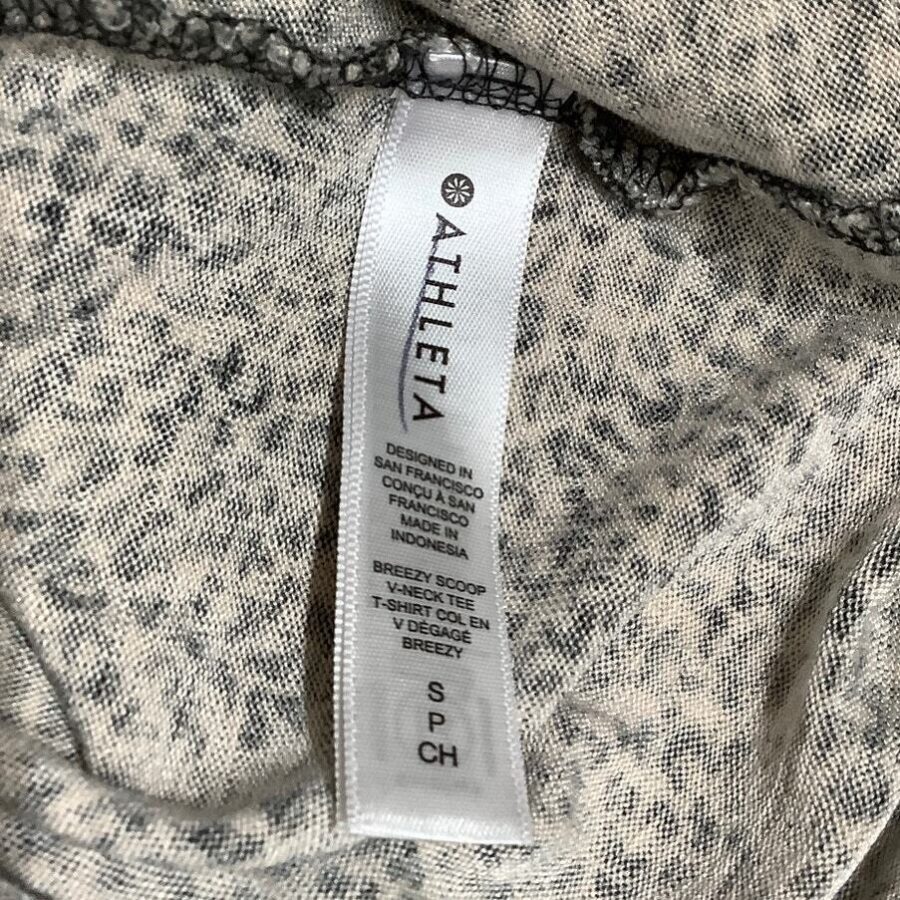 White Athleta clothing tag on a grey fabric, marked "SP/CH," with details about design in San Francisco and manufacturing in Indonesia.