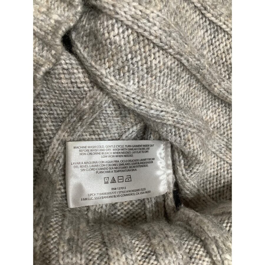 A close-up of a grey knit fabric with a care label instructing machine wash cold, gentle cycle, and other washing instructions in multiple languages.