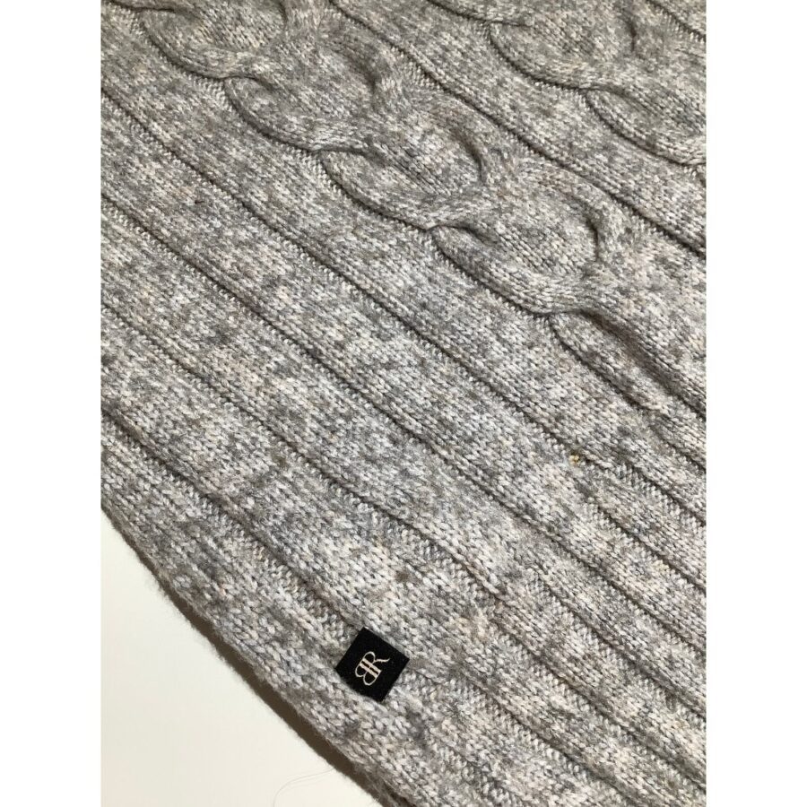 A close-up of a gray cable-knit sweater with ribbed patterns, featuring a small black label with white initials "BR."