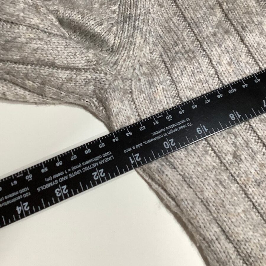 A black ruler measuring around 24 inches is placed diagonally over a grey knitted fabric, possibly a sweater, on a white surface.