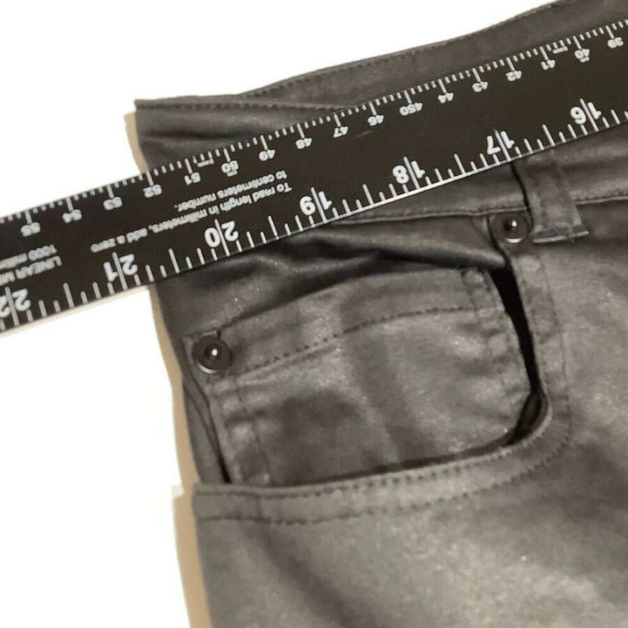 A close-up view of black pants with a black measuring ruler placed on top, showing measurements in inches and centimeters.