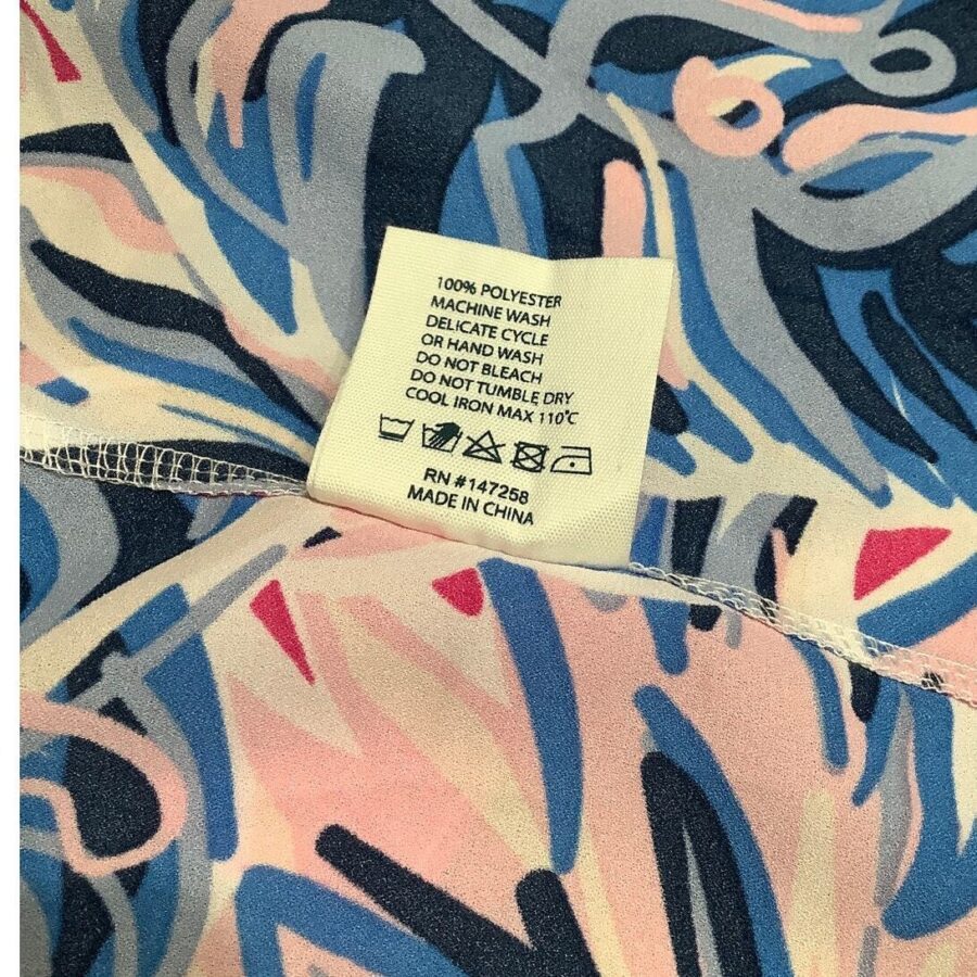 A polyester garment with a colorful abstract pattern; a care label in English provides washing and drying instructions. Made in China.