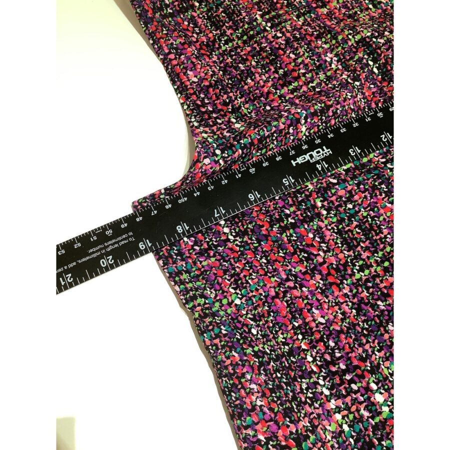 A multicolored fabric with a Hendon ruler measuring its width lies on a surface, featuring a pattern of small, vibrant speckles.