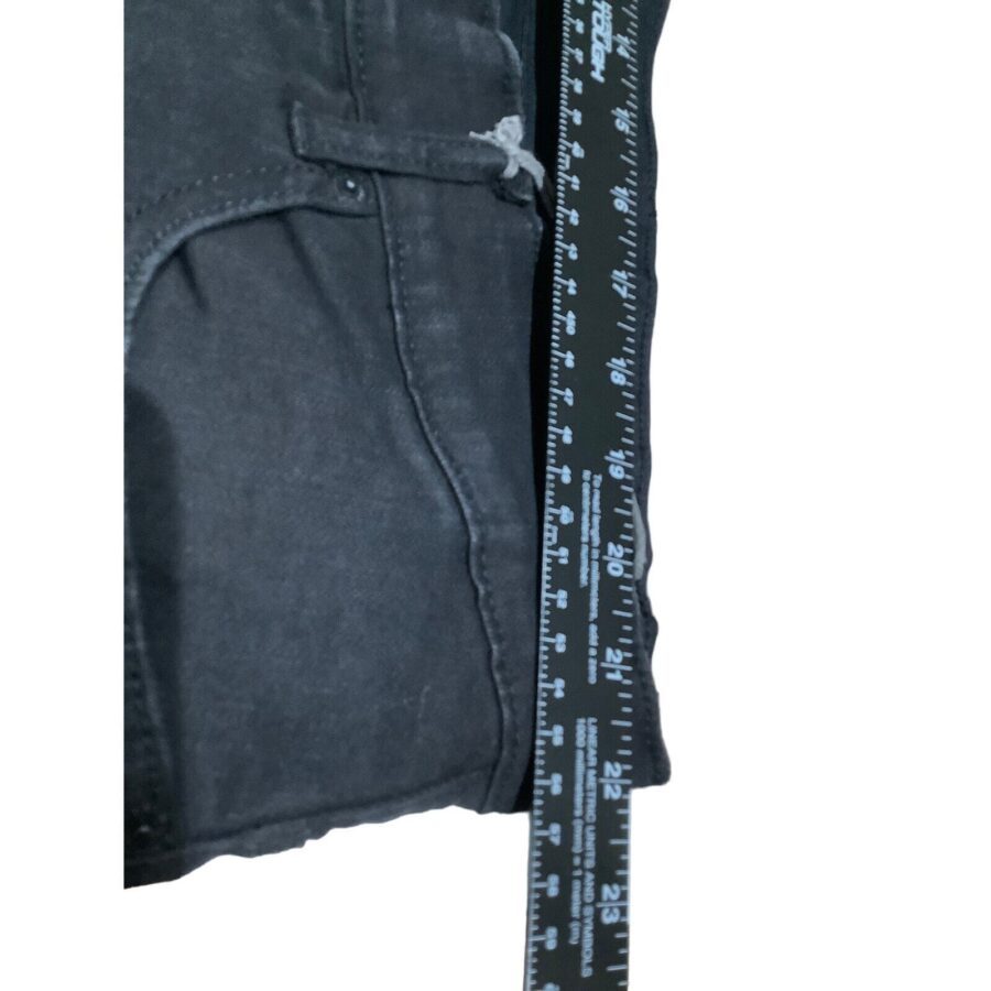 The image shows a close-up of dark jeans next to a black ruler with white markings, measuring approximately 24 inches.