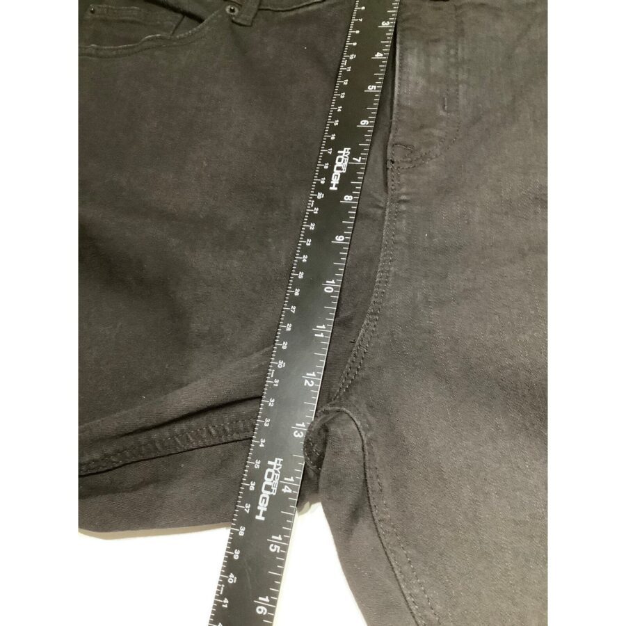 Black pants being measured with a 24-inch ruler placed across the waistband and along the inner seam, displayed on a flat surface.