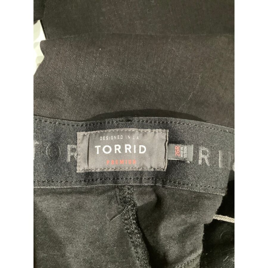 Close-up image of black denim jeans showing the "Torrid Premium" label. The jeans are folded neatly, displaying the waistband and stitching details.