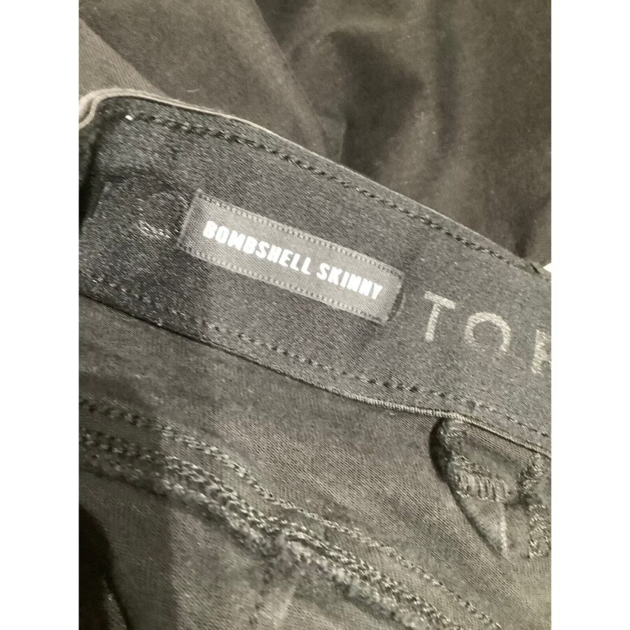 Close-up of dark denim jeans with the label "BOMBSHELL SKINNY" visible, showcasing detailed stitching and texture of the fabric. No recognizable landmarks.