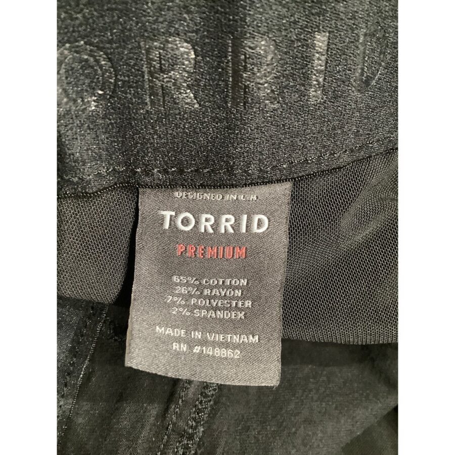 A close-up of a fabric tag on black clothing. The tag reads "TORRID PREMIUM" and details the material composition and country of manufacture (Vietnam).