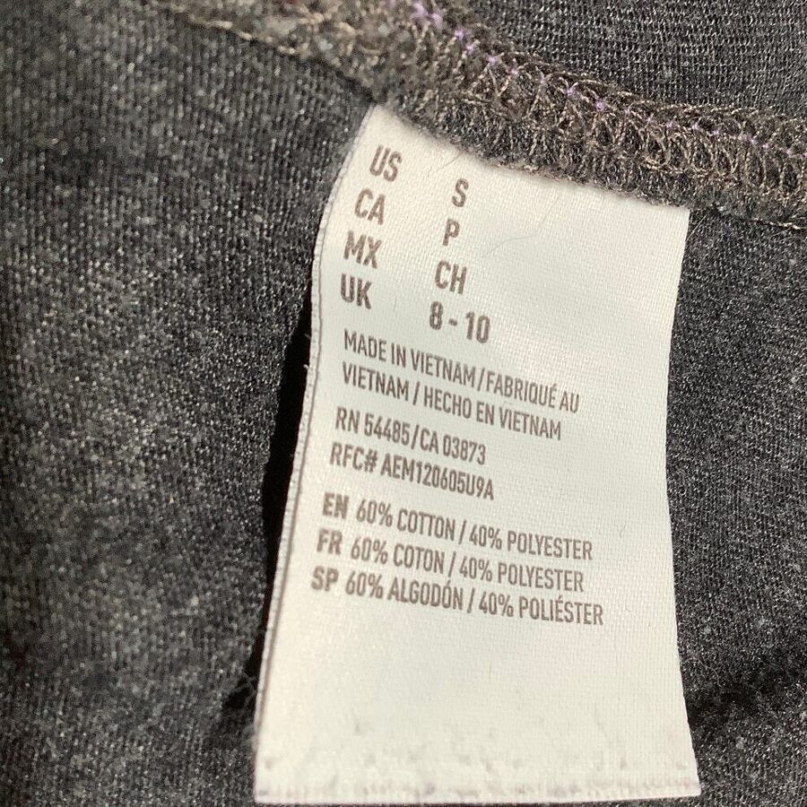 A garment label indicating size "S" and composition (60% cotton, 40% polyester), made in Vietnam, against a dark fabric background.